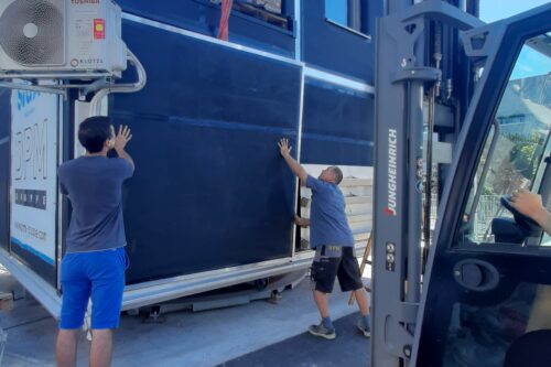 Zwei Mitarbeiter der Firma DPM halten eine Wand und bauen sie mit Hilfe eines Staplers in den Prüfstand ein.