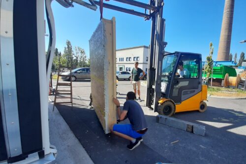 Zwei Mitarbeiter der Firma DPM halten eine Wand und bauen sie mit Hilfe eines Staplers in den Prüfstand ein.