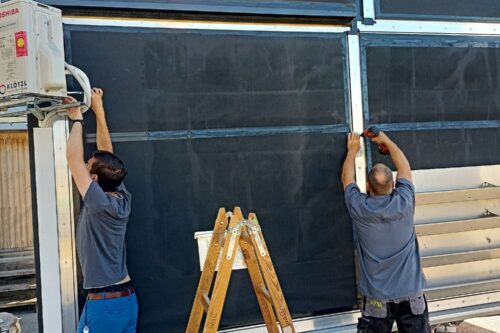 Zwei Mitarbeiter der Firma DPM schrauben eine fertige Wand am Prüfstand ein.